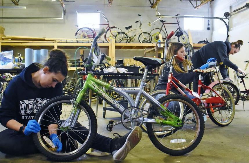 三名365英国上市的学生在圣姐妹学校修自行车. 约瑟夫社区网络自行车仓库.